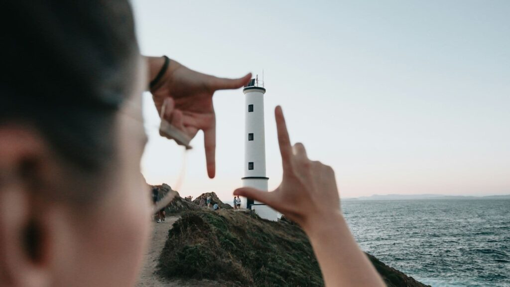 A person framing a lighthouse with their hands, symbolising focus, clarity and direction—reflecting the idea of choosing a personal intent word for the year.