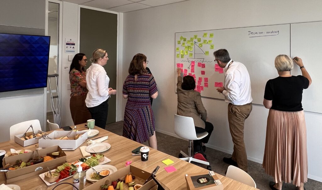 A leadership team participating in a collaborative problem-solving workshop, using sticky notes on a whiteboard to identify challenges and align on shared solutions.
