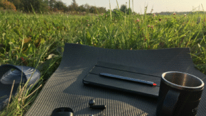 A notebook, pen and coffee mug resting on a mat in a grassy outdoor setting, symbolising quiet reflection, focus and intentional thinking.