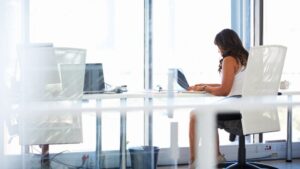 Senior female leader sitting alone at a desk working on a laptop in a bright office space