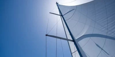 Sailing with the wind at open sea ocean, summer holidays concept. Yacht wind filled sails on clear blue sky background. Looking up at the sky, sun shining, sunbeams on boat rigging, Low angle view